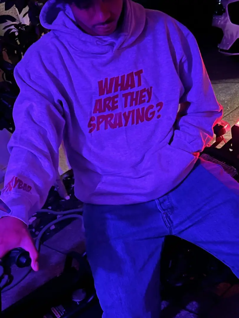 man wearing hoodie with text saying “WHAT ARE THEY SPRAYING?”